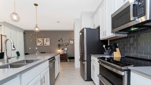 Une cuisine moderne dotée d’appareils électroménagers en acier inoxydable, d’un îlot central et de luminaires suspendus.
