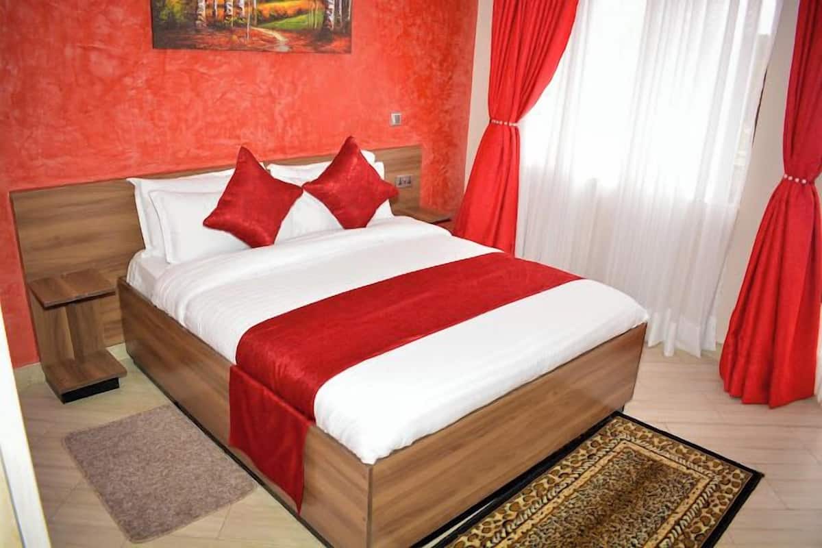 Ein Hotelzimmer mit einem hölzernen Bett, roter Bettwäsche, einem roten Vorhang und einem Gemälde an der Wand.