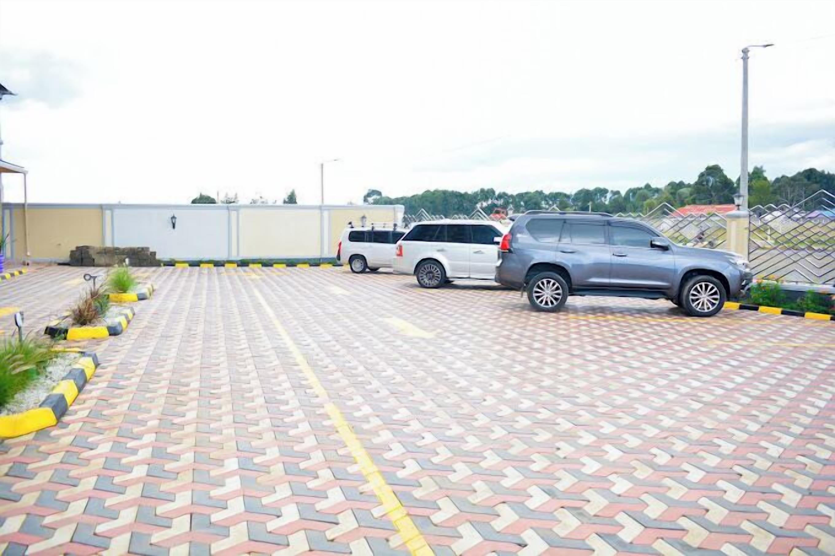 A parking lot with two SUVs parked, paved with interlocking red and beige tiles, and bordered by a low yellow and black curb.
