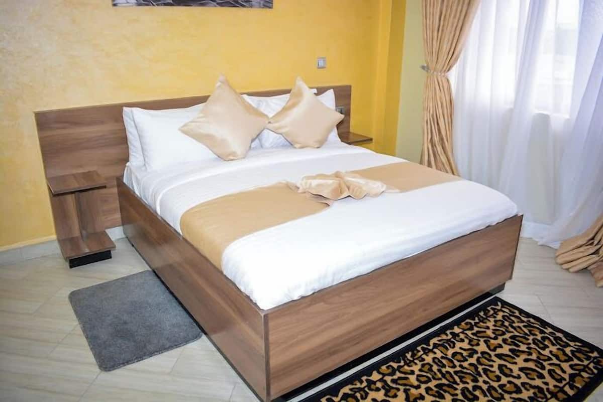 Ein ordentlich bezogenes Bett mit hölzernem Kopfteil, einem grauen Teppich und einer Matratze mit Leopardenmuster am Fußende.