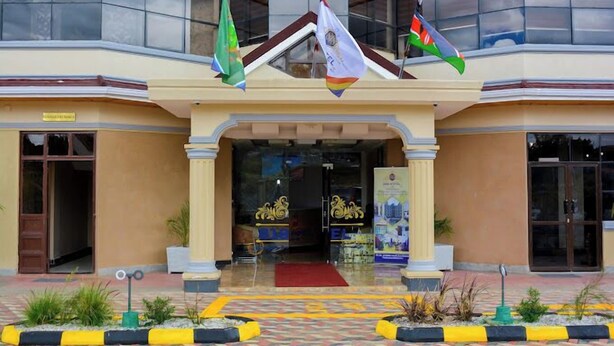 L’entrée d’un hôtel, avec un tapis rouge, plusieurs drapeaux et une porte en verre.
