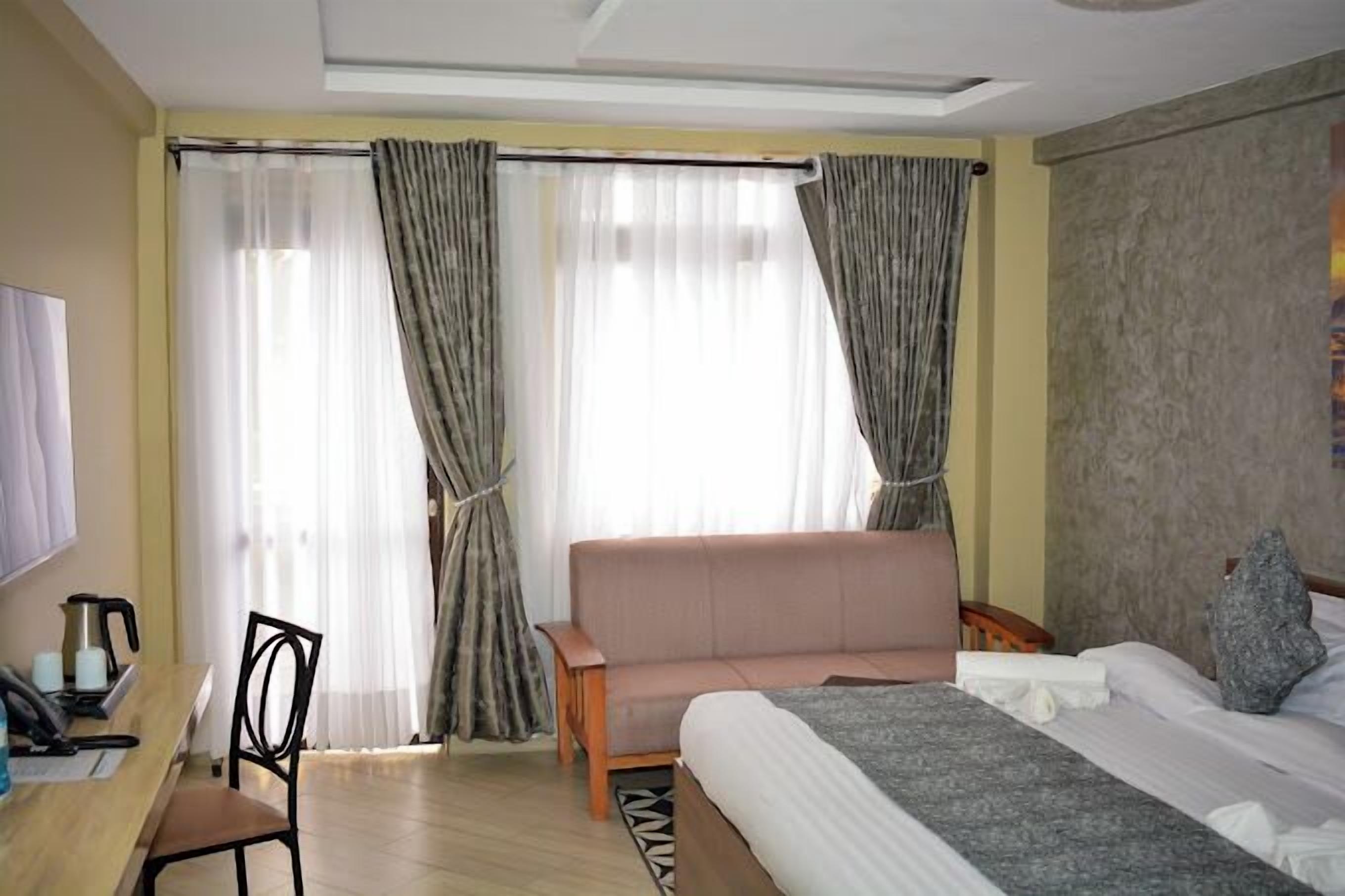 Een hotelkamer met een bed, een bank, een bureau met telefoon en gordijnen.