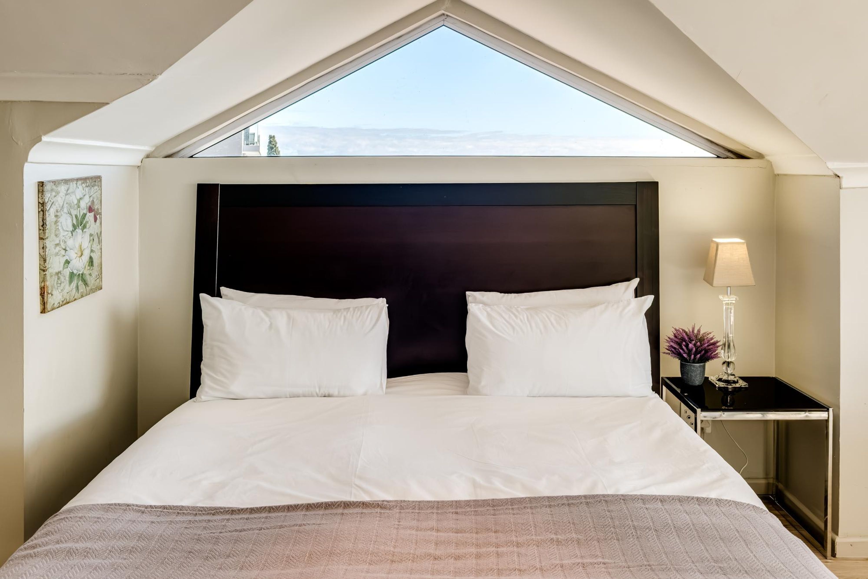 A hotel room with a large bed, a nightstand, a lamp, and a view through a skylight.