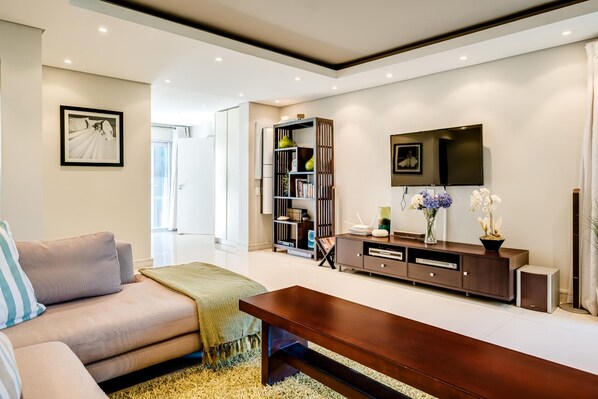 A modern living room with a sofa, a coffee table, a bookshelf, a flat-screen TV, and a decorative vase.