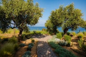 A garden with a gravel path, two chairs, and a view of the sea.