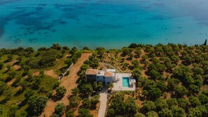Vista aérea de una propiedad costera con piscina, rodeada de abundante vegetación y una vista despejada al mar.