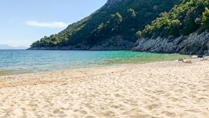 A sandy beach with clear turquoise water and a rocky cliff with greenery. - Pergamonto Cottage - Seaview Nest w Private Pool (Skopelos)