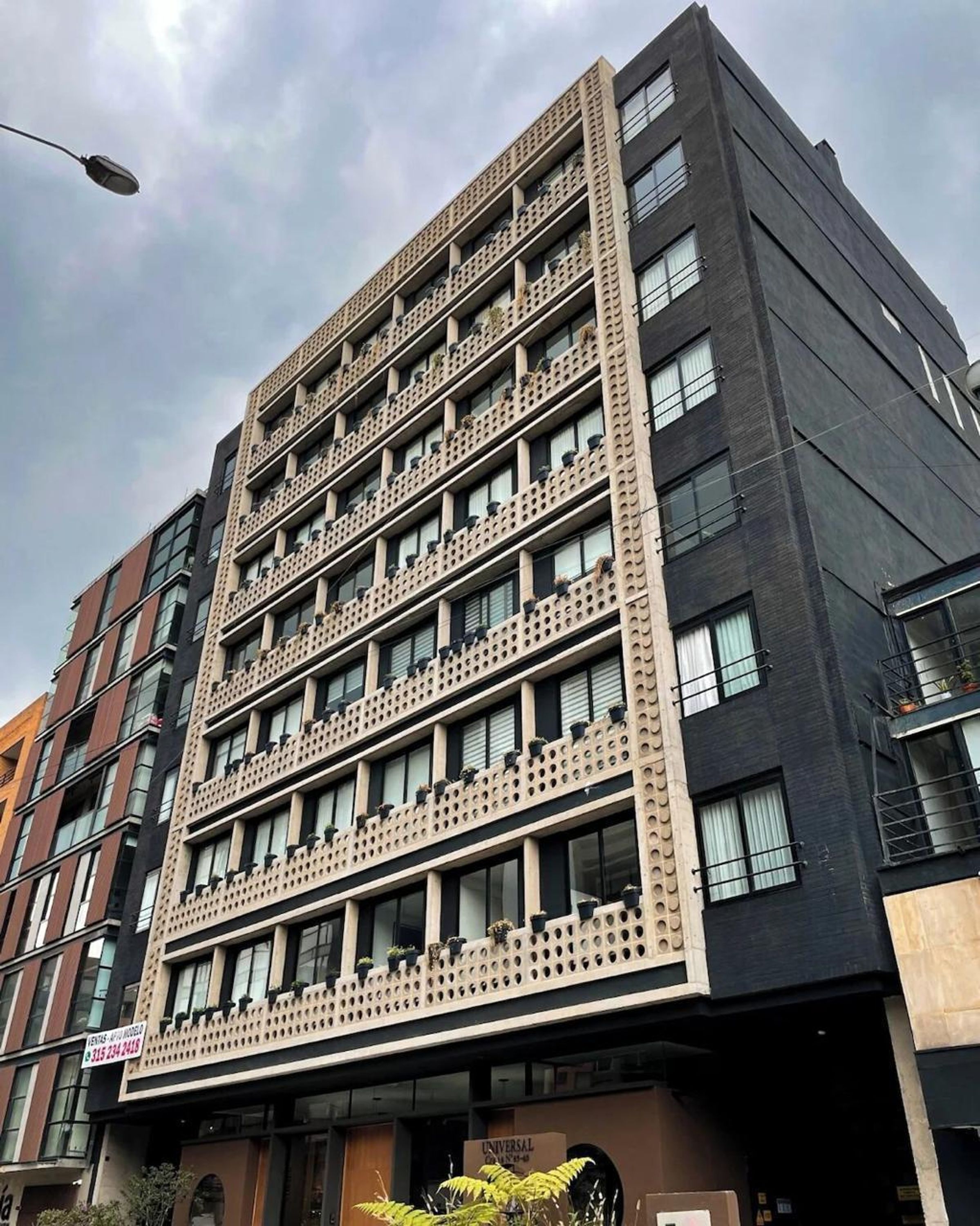 A multi-story building with a modern architectural design, featuring balconies with potted plants and a mix of window styles.