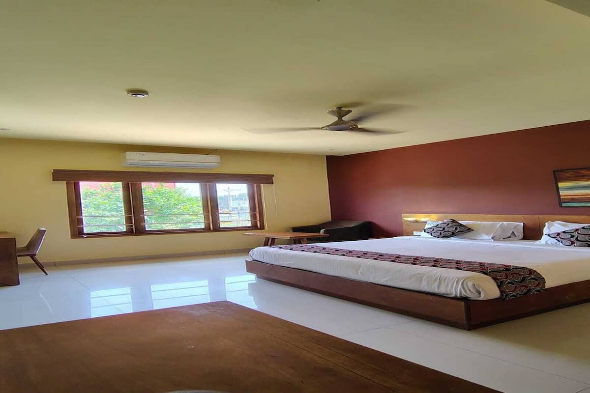 A hotel room with a large bed, a desk, a chair, and a window with a view of greenery.