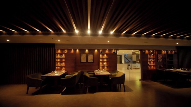Un restaurante tenuemente iluminado con una decoración moderna, que cuenta con una larga mesa de comedor y sillas, y una iluminación cálida.
