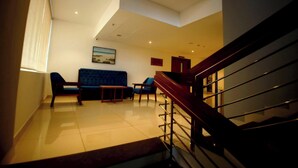 Un salón espacioso con un sofá azul, dos sillones y una pequeña mesa. Una escalera de madera conduce a un piso superior.