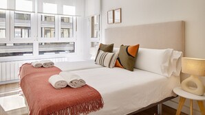 A hotel room with a large bed, a bedside table with a lamp, and a window with blinds. - Izpizua II | The Rentals Collection (San Sebastián/Donostia)