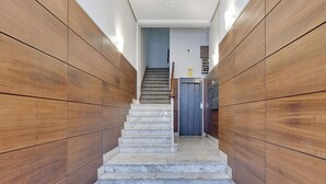 A narrow hallway with wooden paneling on both sides and a marble staircase leading to a door at the end. - Izpizua II | The Rentals Collection (San Sebastián/Donostia)