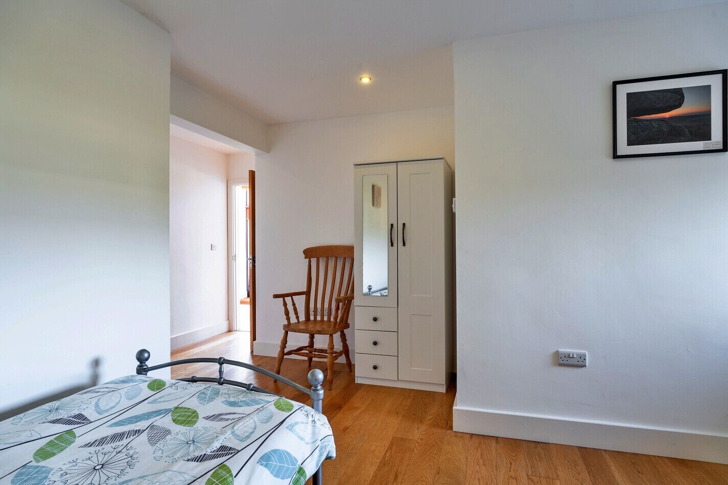 A bedroom with a bed, a wooden chair, a wardrobe, and a framed picture on the wall.