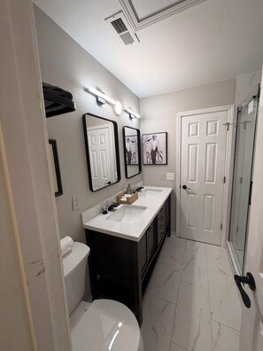 Un baño con dos lavamanos, un inodoro, una ducha y una puerta con cabina de vidrio.