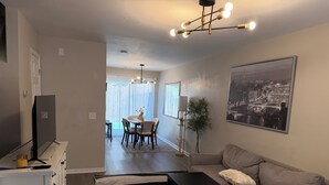 A modern living room with a sofa, a coffee table, and a TV on a stand. There is a dining area with a table and chairs visible in the background. - Charming 2-bedroom townhome with WiFi and AC in Charlotte University Area (Charlotte)