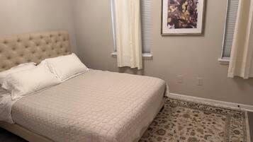 Un dormitorio con cama, cabecero tapizado, alfombra estampada y un cuadro enmarcado en la pared.