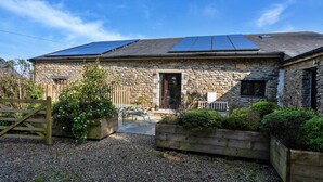A stone house with a gravel driveway, a wooden gate, and solar panels on the roof. - Jubilee Barn Cottage at Bodmin Moor (St Breward)