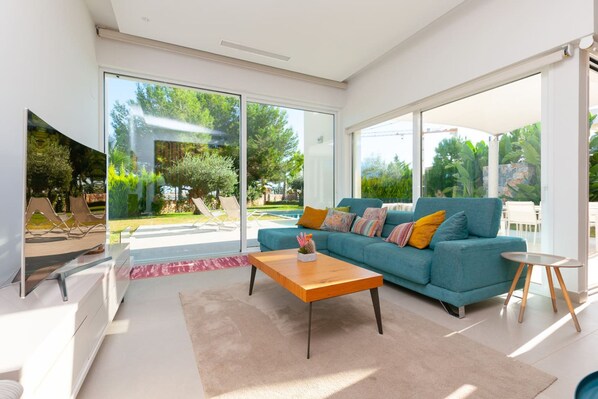A modern living room with a blue sofa, a wooden coffee table, and a TV on a white cabinet. - Sisu Willa z Podgrzewanym Basenem Las Colinas Golf (Orihuela)