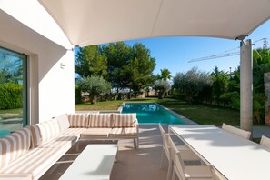 A modern outdoor seating area with a pool, featuring a white table and striped cushions. - Sisu Willa z Podgrzewanym Basenem Las Colinas Golf (Orihuela)