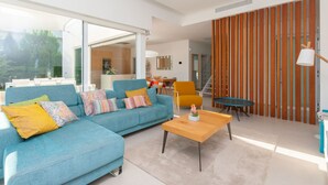 A modern living room with a blue sofa, a wooden coffee table, and a yellow armchair. There is a large window providing natural light and a view of the outdoors. - Sisu Willa z Podgrzewanym Basenem Las Colinas Golf (Orihuela)