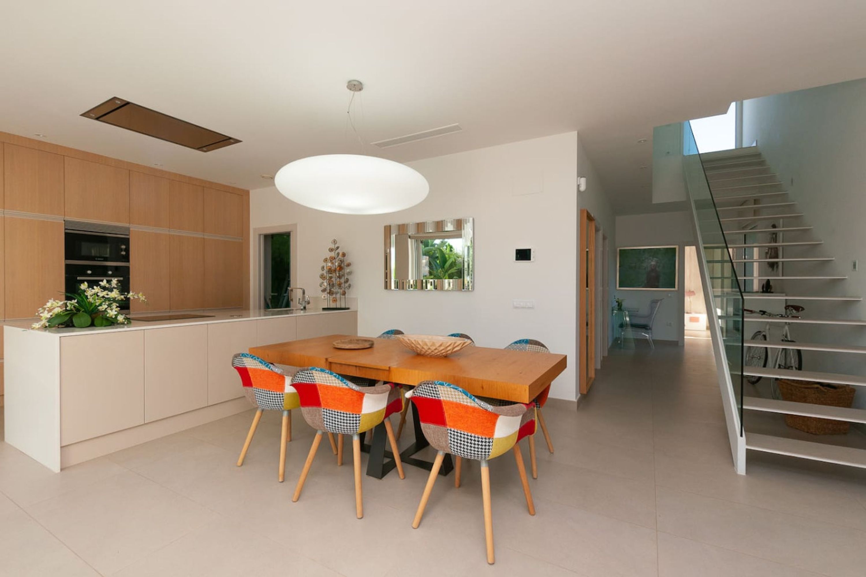 Una cocina moderna con comedor, armarios de madera, una isla grande y una escalera que sube a un nivel superior.