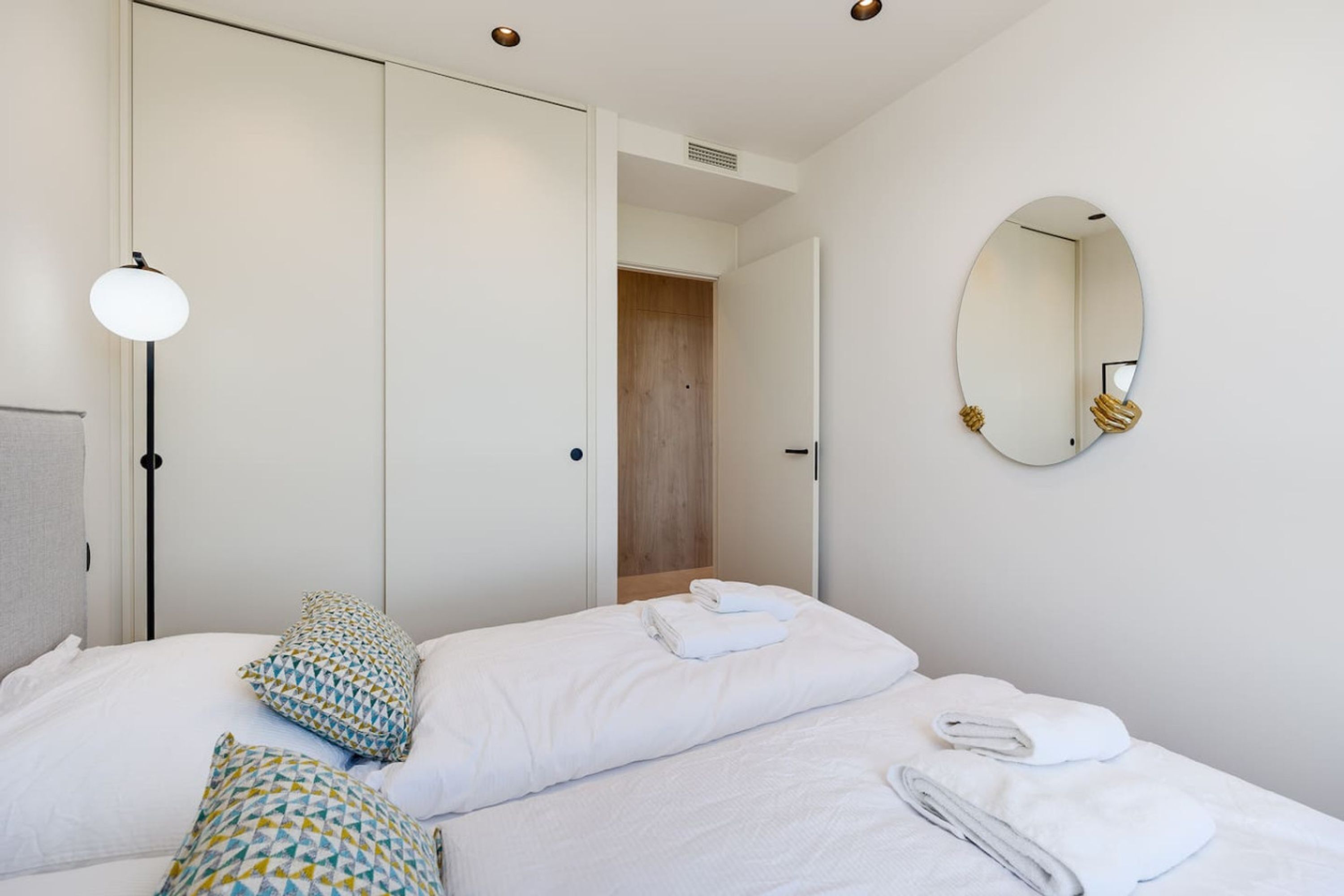 Ein Hotelzimmer mit einem Bett, Kissen, einer Nachttischlampe, einem Spiegel und einer Tür zu einem Badezimmer.