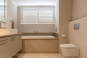 Une salle de bain moderne avec une baignoire, des toilettes et une fenêtre équipée de stores.
