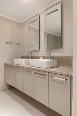 Une salle de bain moderne avec deux lavabos, un grand miroir et un porte-serviettes.