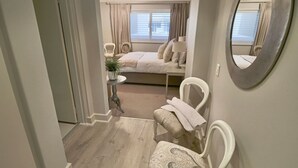 A bedroom with a bed, a chair, a small table with a plant, and a mirror on the wall. - Bantry Place - Luxury Apartment (Cape Town)