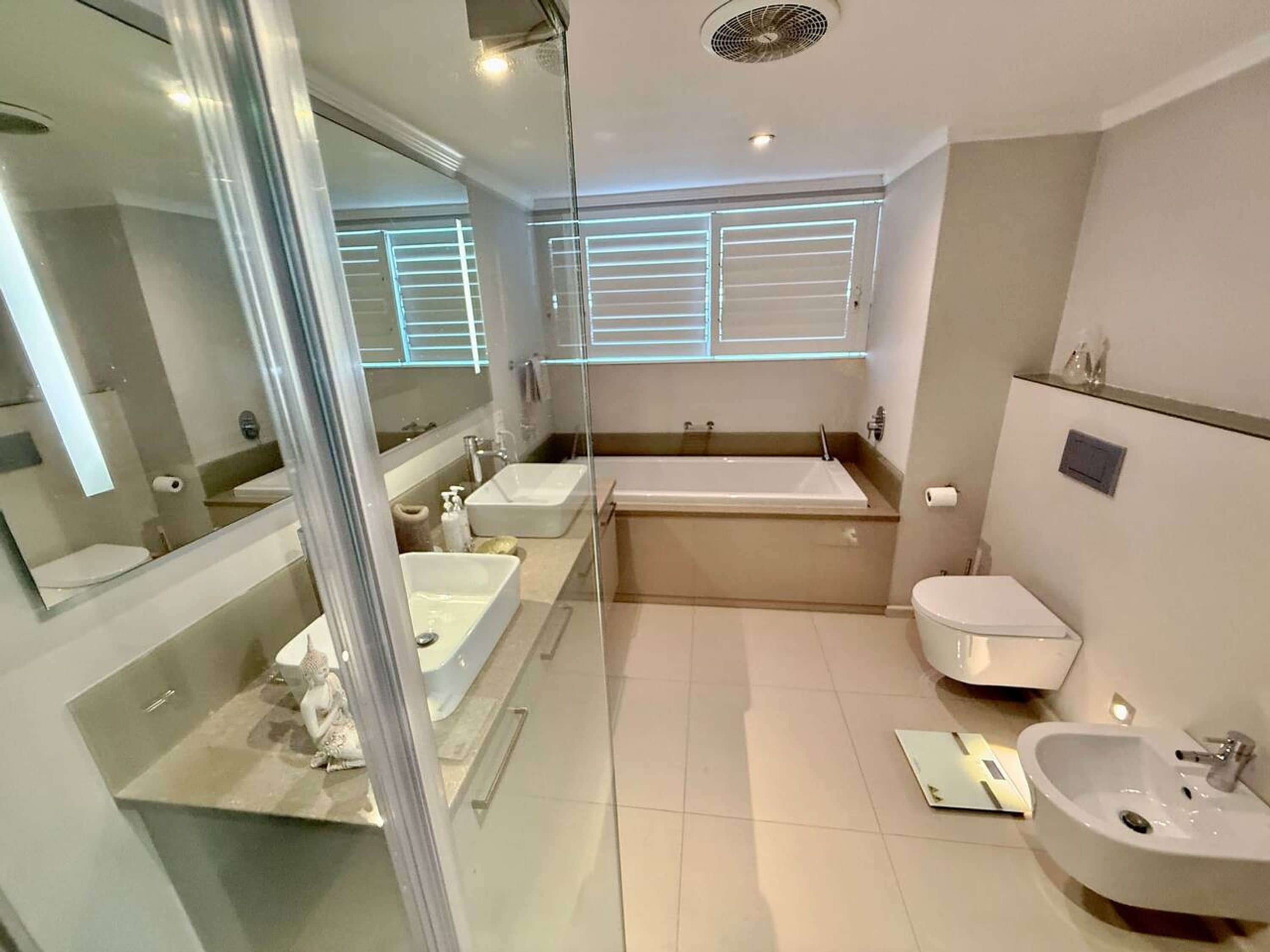 A modern bathroom with a bathtub, two sinks, a toilet, and a glass shower enclosure.
