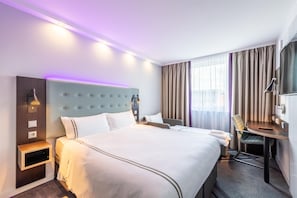 Hotellihuone, jossa on suuri sänky, yöpöydät, työpöytä ja tuoli.
