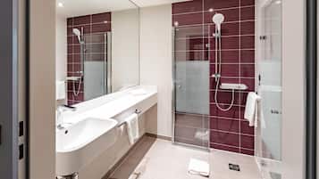 Ein modernes Badezimmer mit einer begehbaren Glasdusche, einem weißen Waschbecken und einem großen Spiegel.