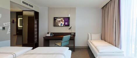 Habitación de hotel con dos camas individuales, un escritorio con silla, televisión y un ventanal con cortinas.