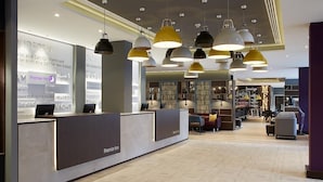 A hotel reception area with a modern design, featuring a reception desk, multiple seating areas, and a visible lounge area in the background. - Premier Inn Frankfurt Messe (Frankfurt)