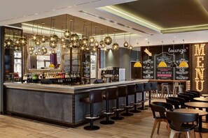 A bar area with a counter, stools, and hanging lights. - Premier Inn Frankfurt Messe (Frankfurt)