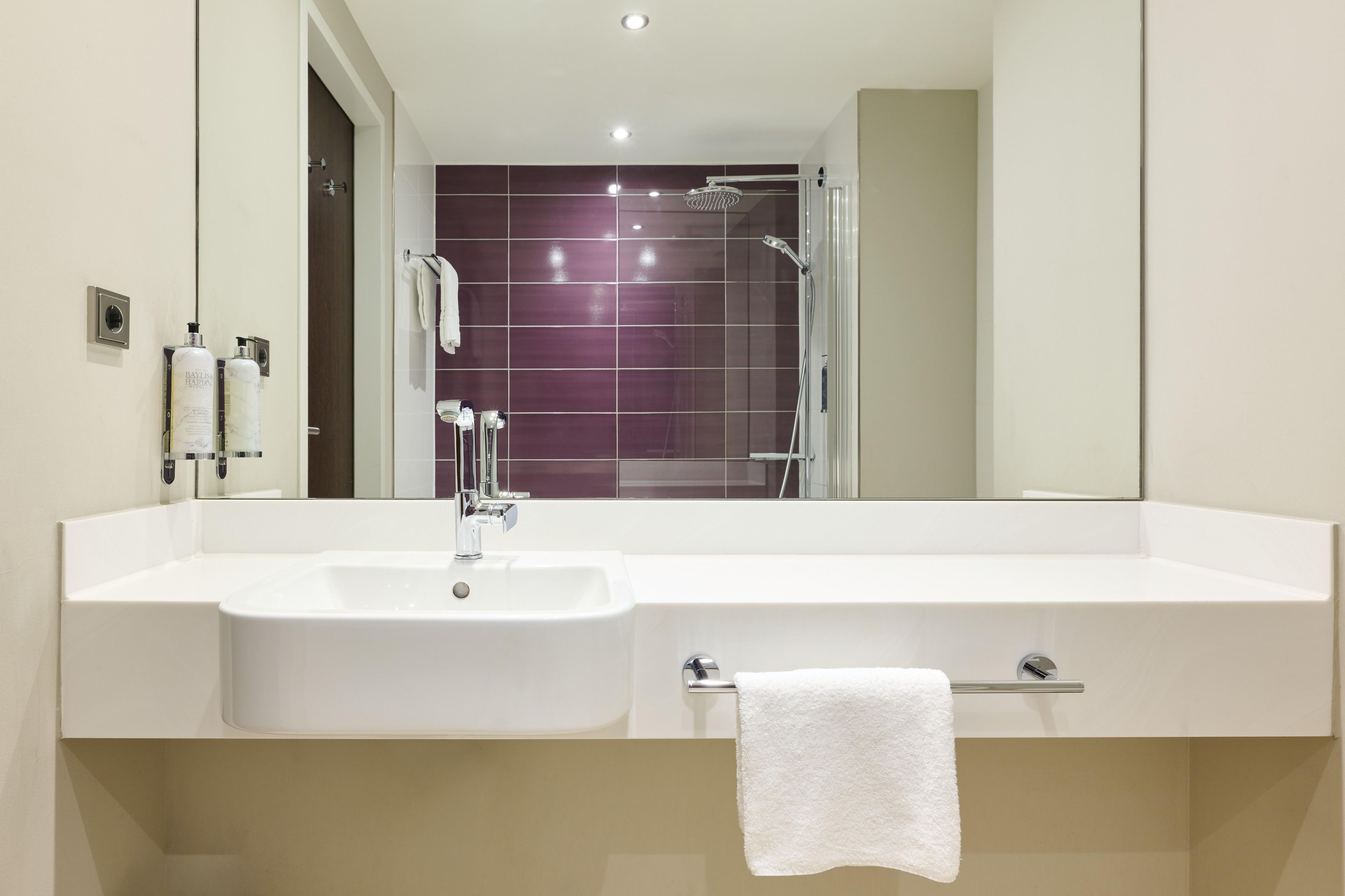 Un baño moderno con lavamanos blanco, un espejo, cabina de ducha de vidrio y un perchero para toallas.