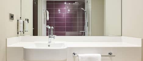 A modern bathroom with a white sink, a mirror, a glass shower enclosure, and a towel rack.