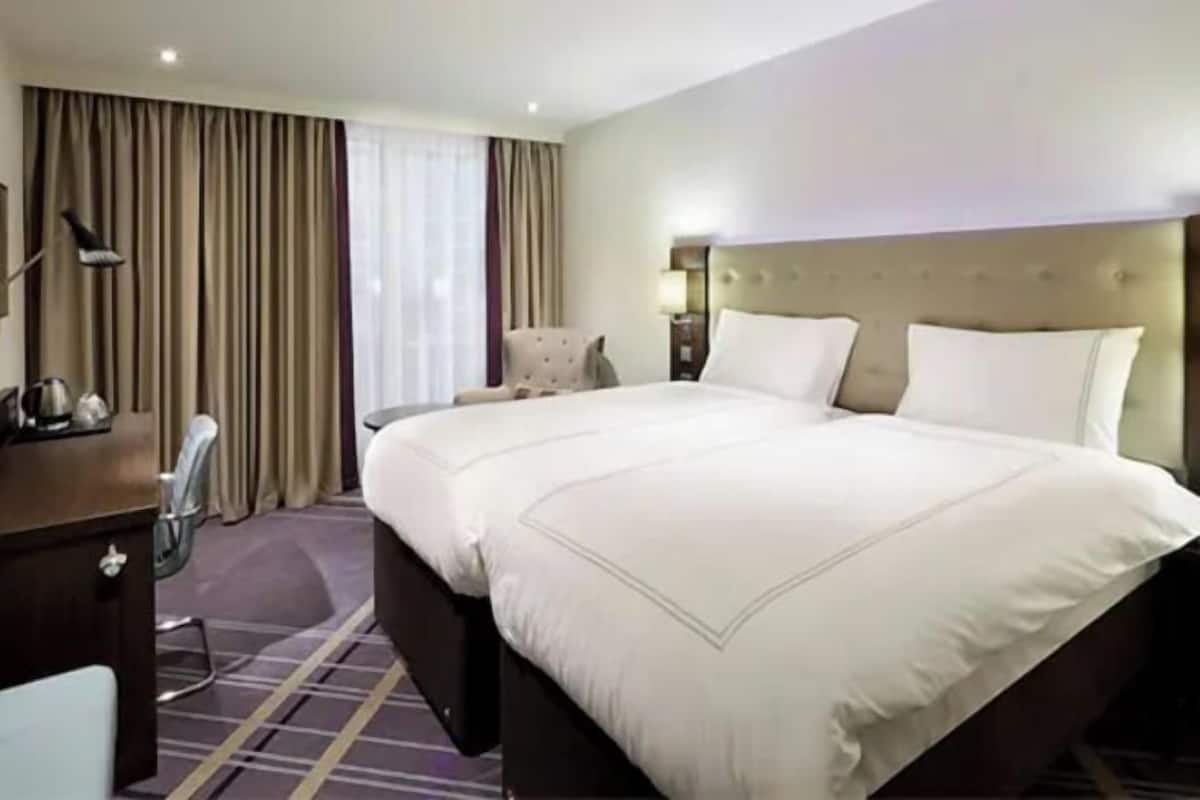 Una habitación de hotel con una cama grande, un escritorio, una silla y una ventana con cortinas.
