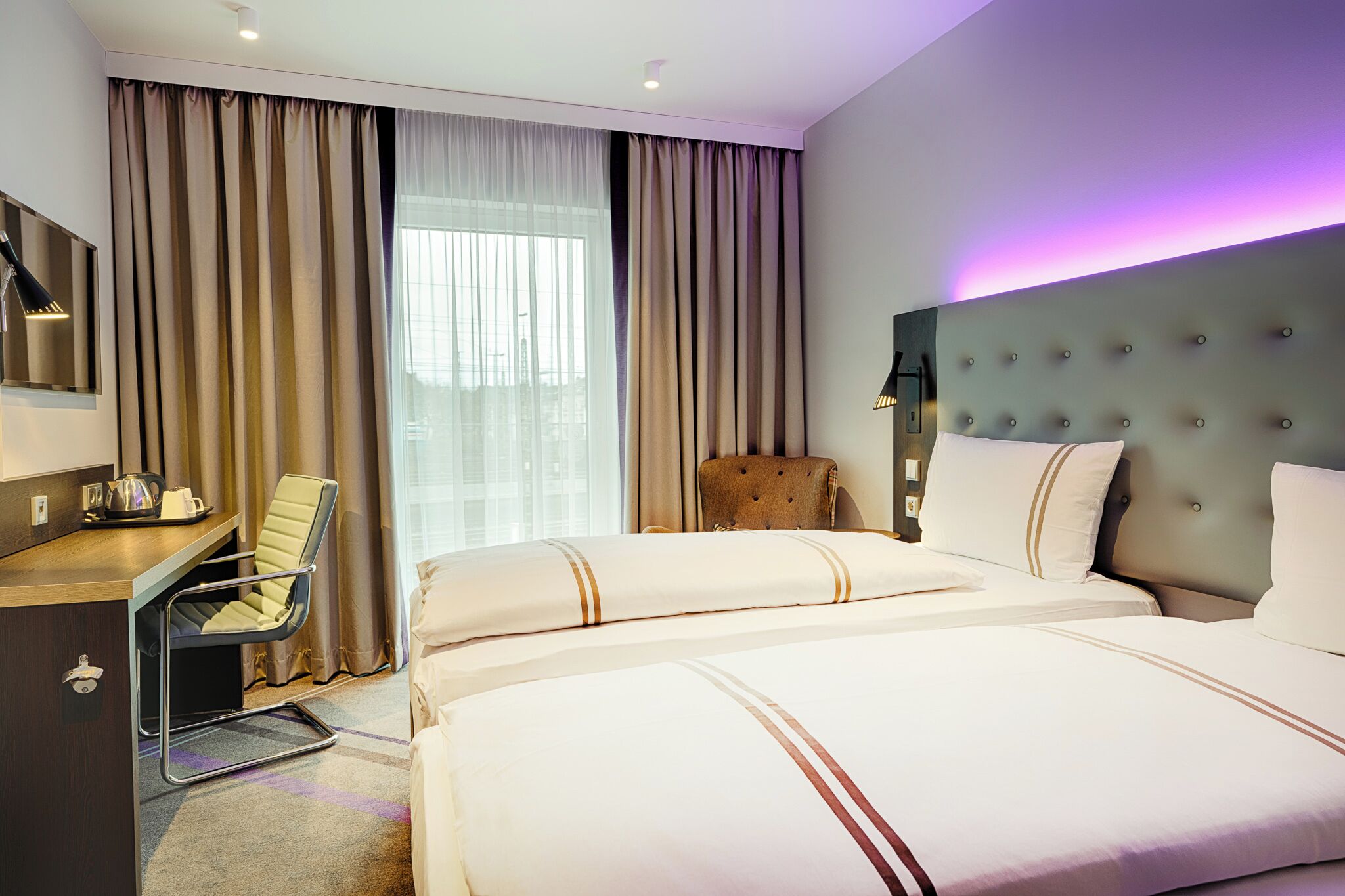 A hotel room with a bed, a desk, a chair, and a large window with curtains.