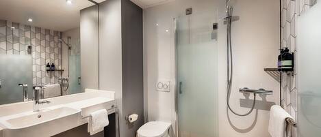 Un baño moderno con un espejo grande, un lavamanos, un inodoro y una zona de ducha con mampara de vidrio.