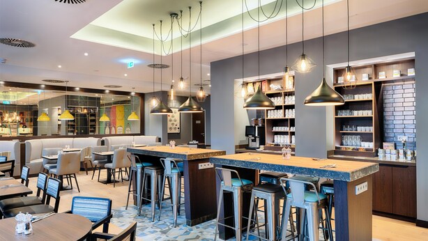 Zona de bar moderna con taburetes altos, iluminación colgante y mostrador.