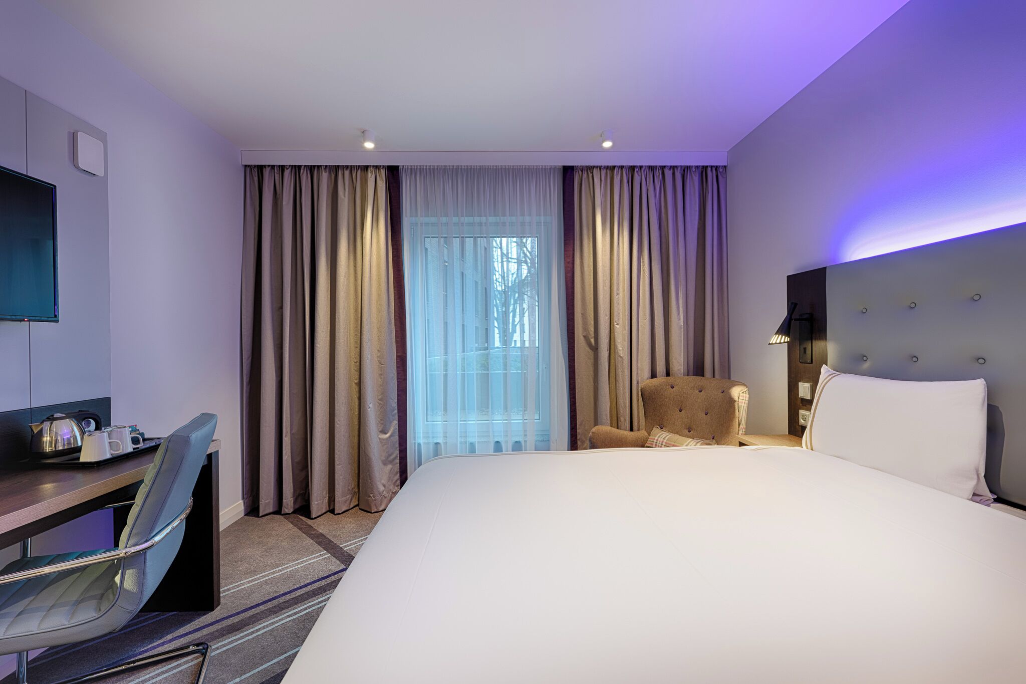 Habitación de hotel con una cama grande, un escritorio con silla, televisión y una ventana con cortinas.