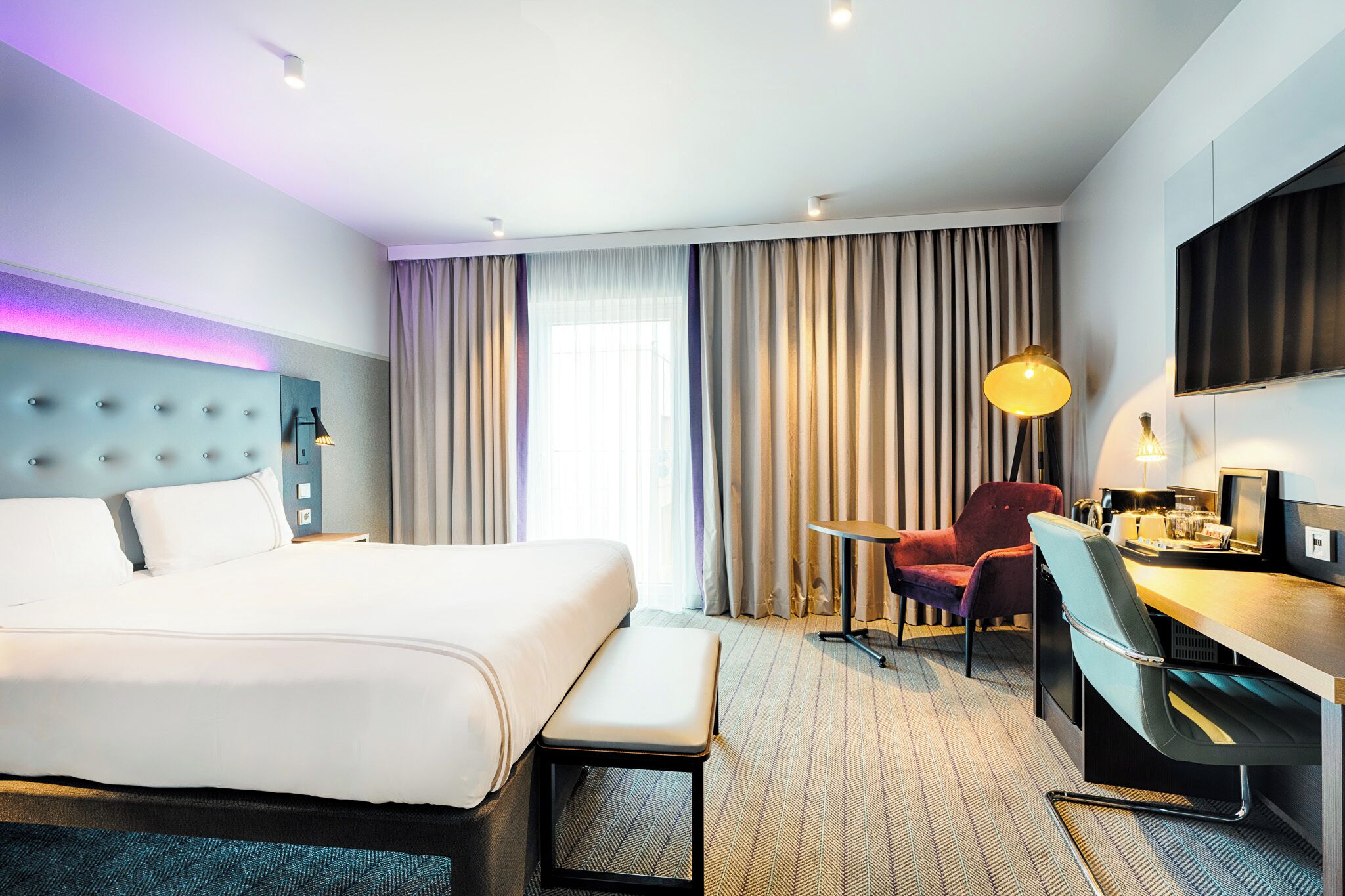Una habitación de hotel con una cama grande, un escritorio, una silla, una mesita y un televisor.