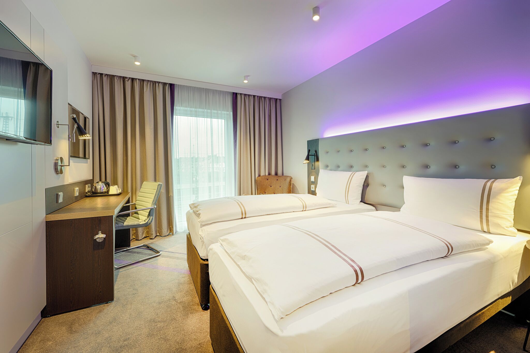 Una habitación de hotel con cama, escritorio, silla, televisor y ventana con cortinas.
