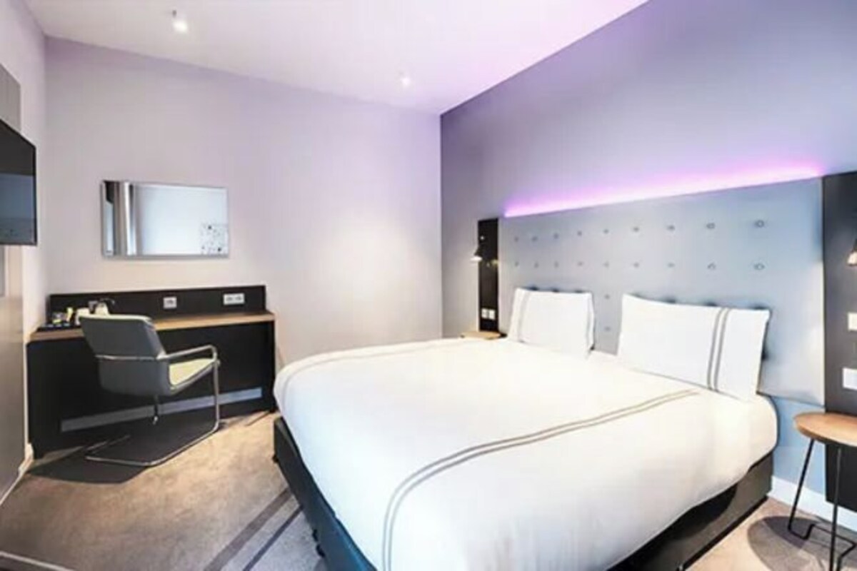 A modern hotel room with a large bed, a desk, and a chair.