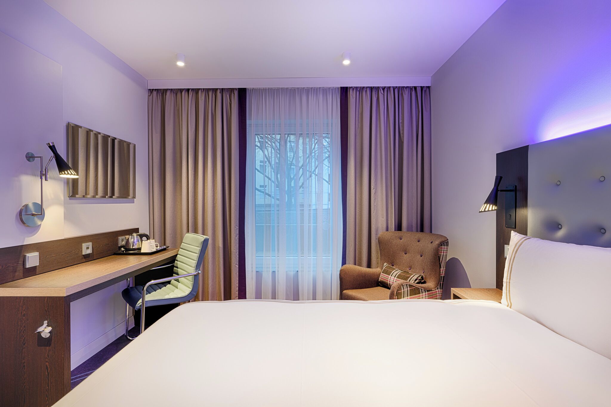 Habitación de hotel con cama, escritorio, silla y vistas al exterior por la ventana.