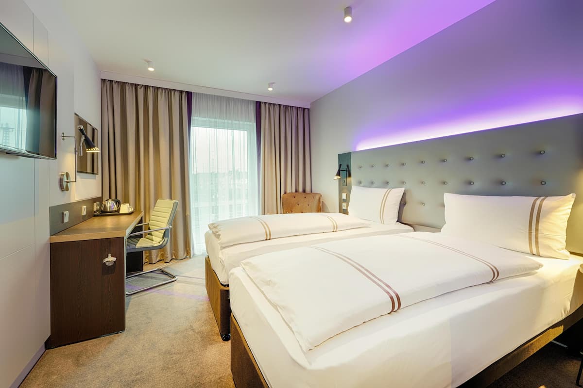 Una habitación de hotel con una cama grande, un escritorio con una silla, un televisor y una ventana con cortinas.
