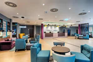 A modern lobby with seating areas, a reception desk, and a bookshelf. - Premier Inn Düsseldorf City Friedrichstadt (Düsseldorf)