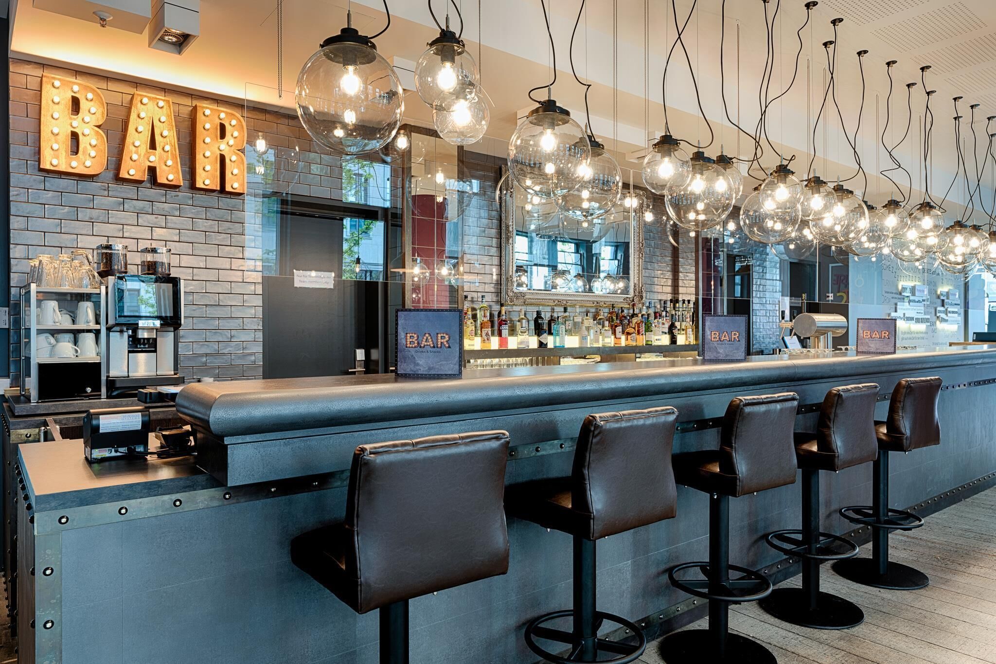 A bar area with a brick wall, bar stools, and hanging light fixtures.